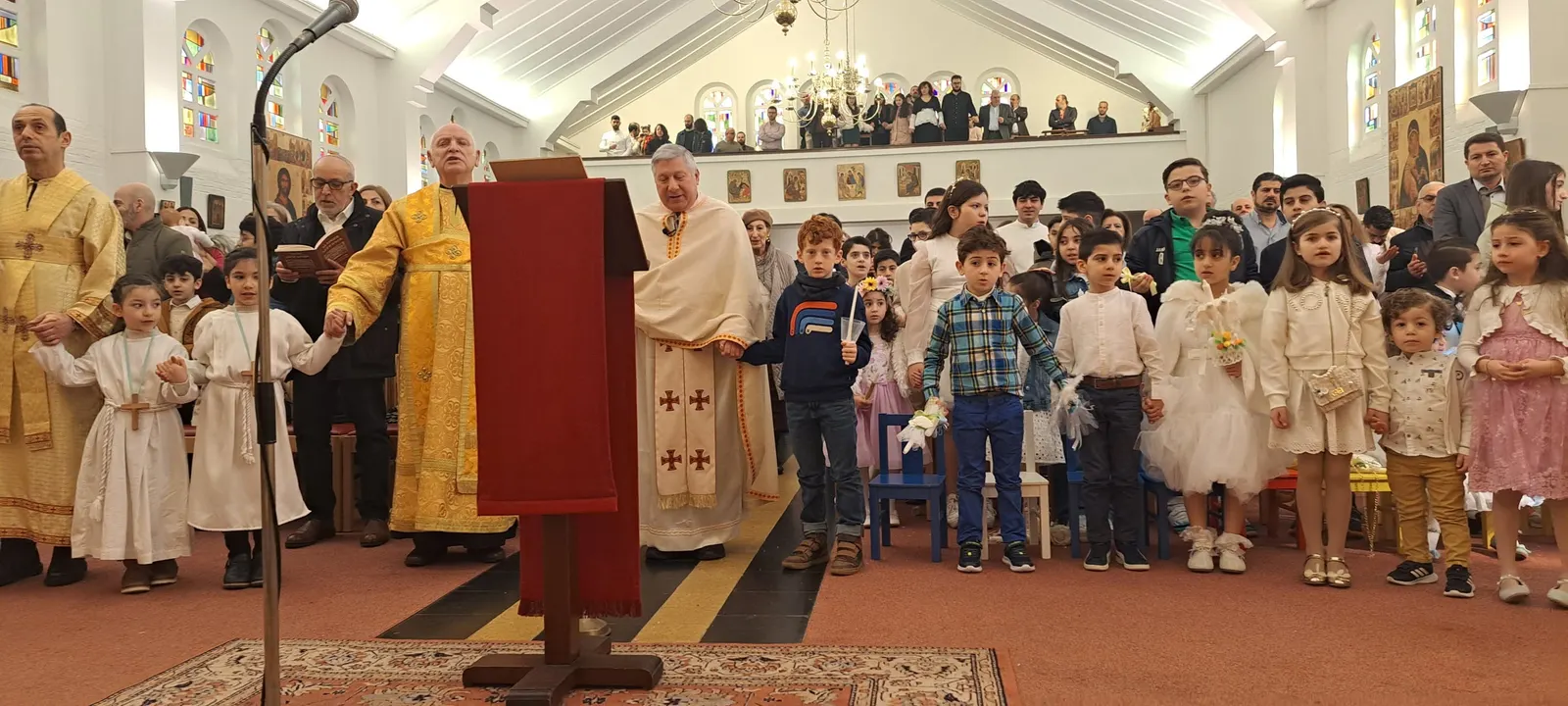 Le P. Antoine Tannous et les prêtres, avec les enfants de la paroisse qui se tiennent par la main pendant la Divine Liturgie